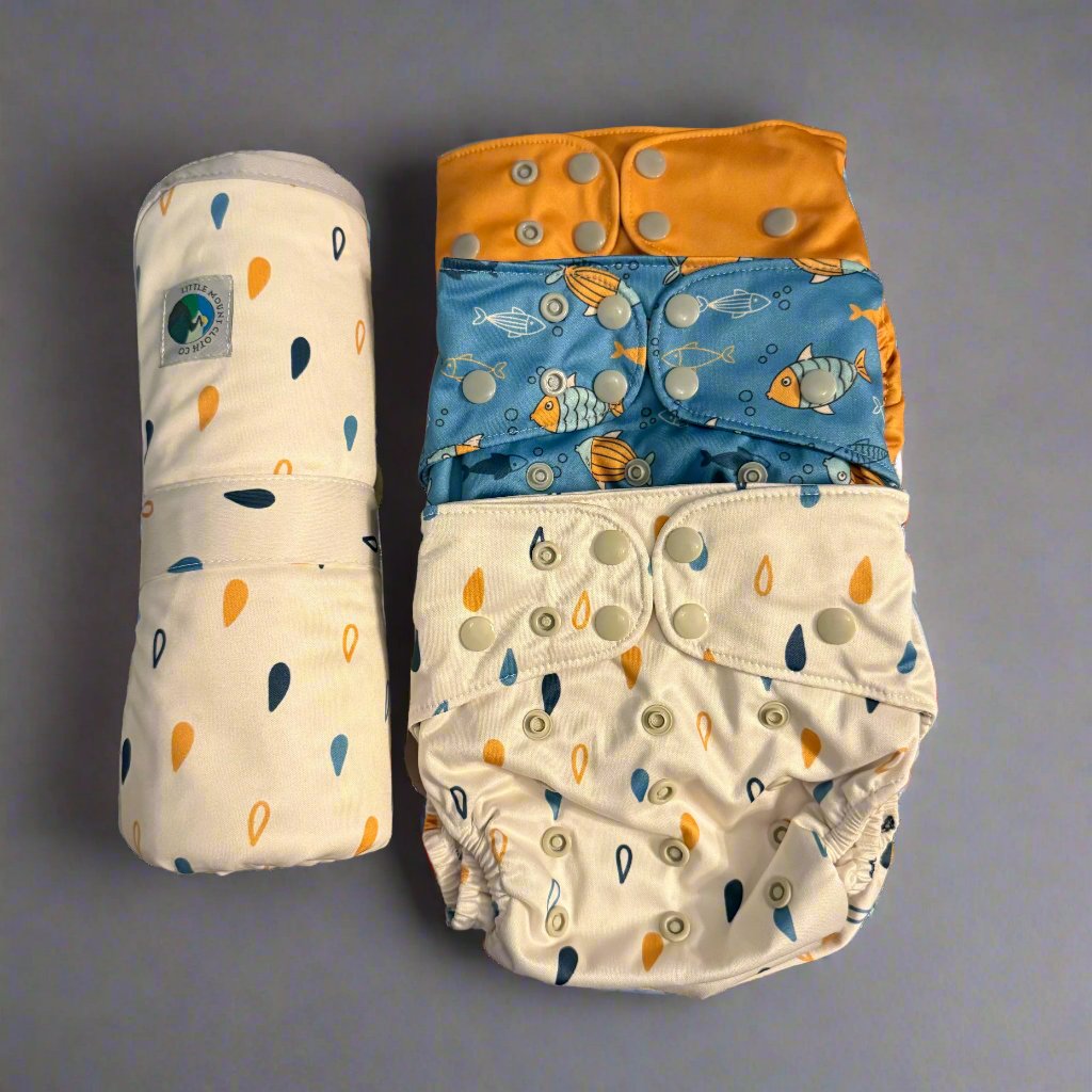 product bundle with change mat with rain drops in yellow and blue with off-white background; three cloth diapers: one yellow; one blue with fish; and one with yellow and blue raindrops; 