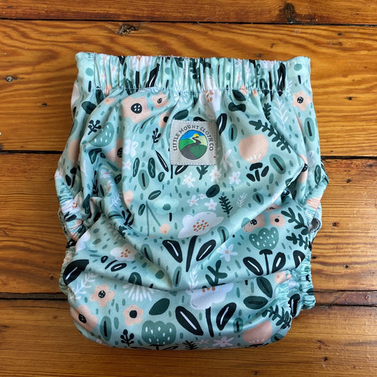 A reusable cloth diaper with gray lining, floral folk art print with teal background on the outer PUL. Light Gray snaps.